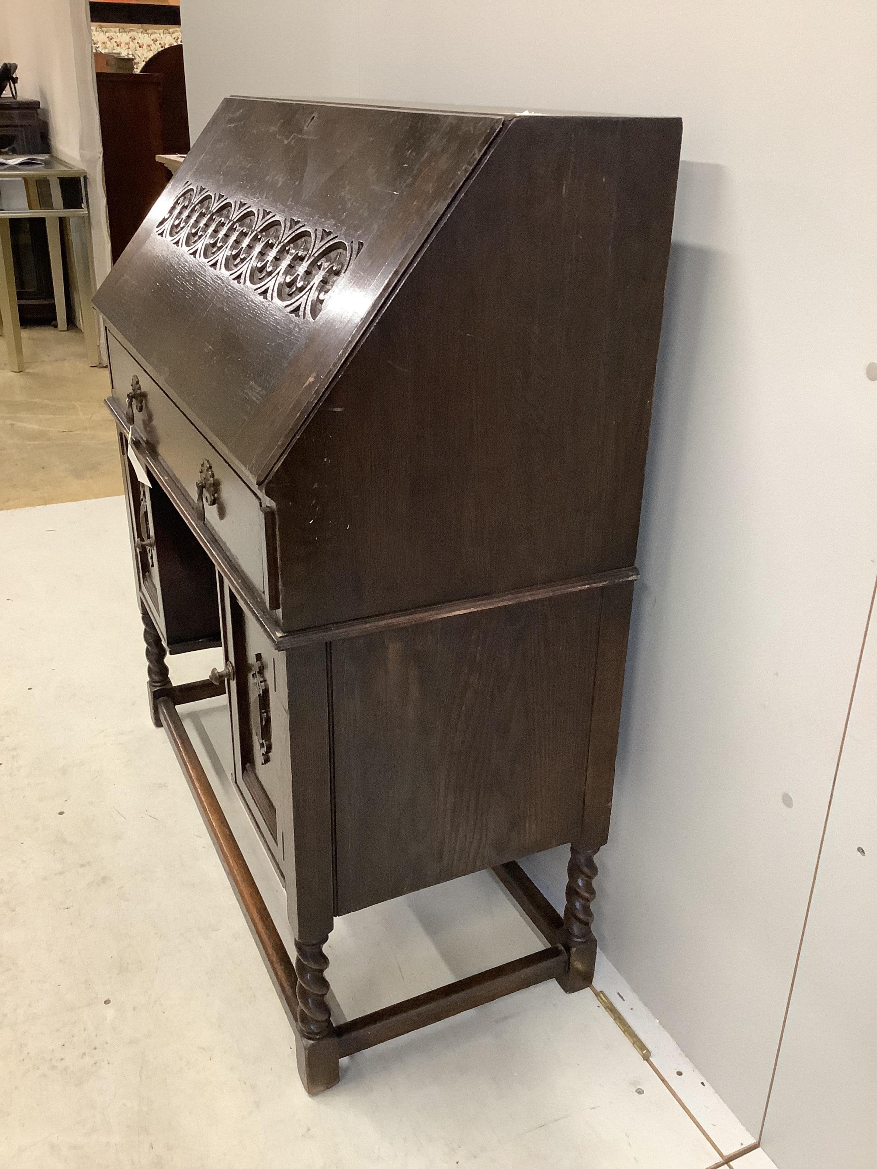 A dark oak Tudor style bureau with a decorative carved front, single drawer above cupboard doors, width 91cm, depth 42cm, height 109cm. Condition - fair